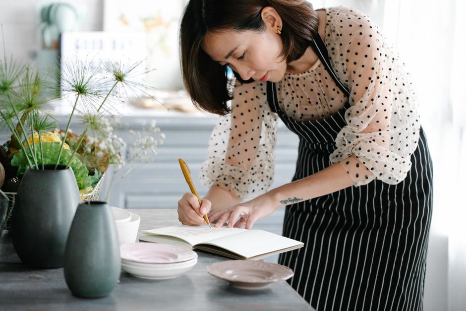 Focused woman in apron writing recipes in a cookbook in a stylish kitchen.